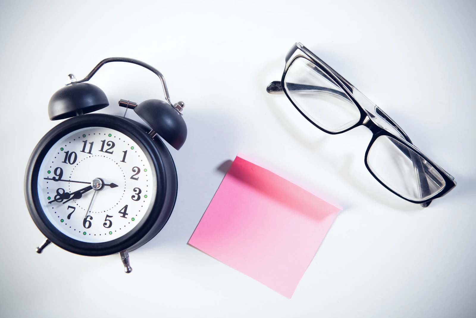 An alarm clock beside glasses and a note
